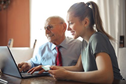 Elderly man and young lady at laptop holding bank card