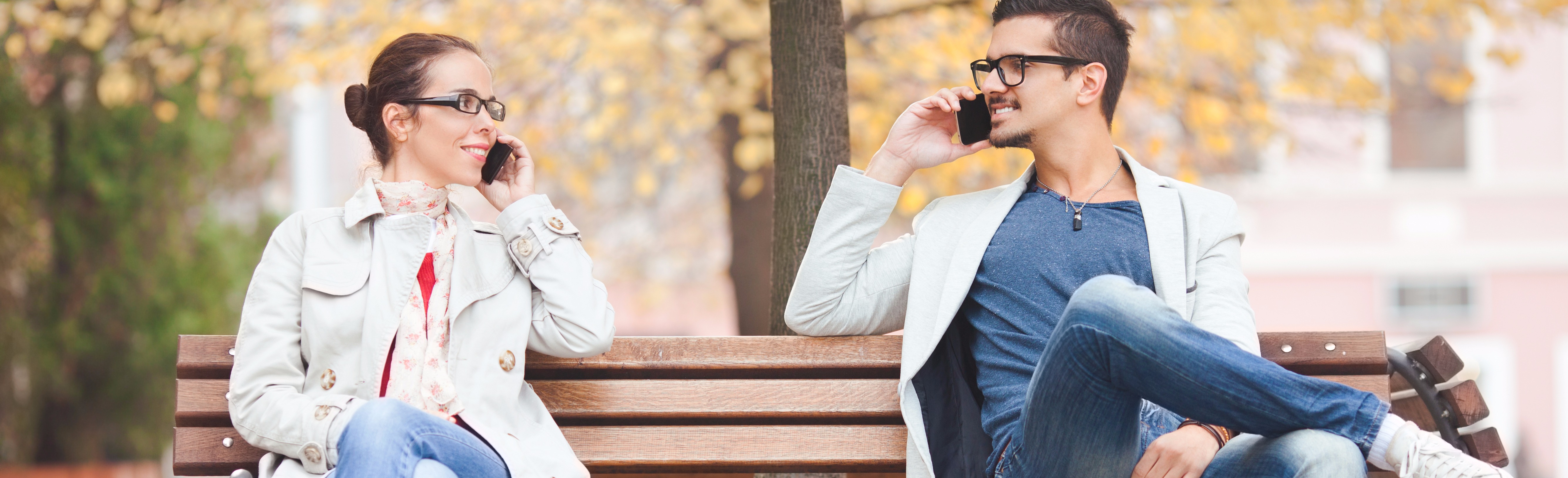 Couple sitting on park bench talking on phone