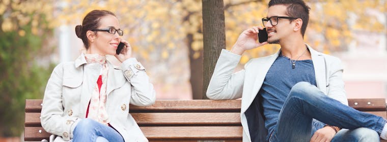 Couple sitting on park bench talking on phone