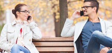 Couple sitting on park bench talking on phone