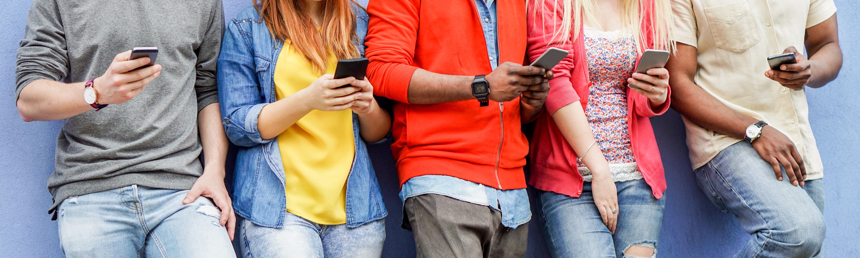 Group of young people standing against a wall using mobile phones